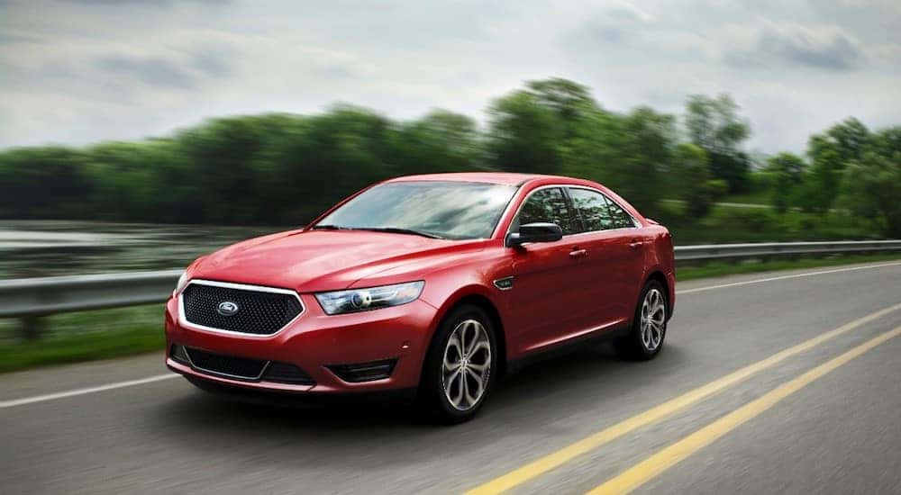 Red 2017 Ford Taurus sedan driving down a paved road past green trees