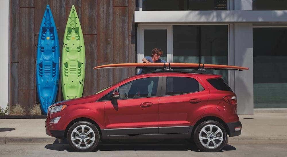 A red 2020 Ford EcoSport is parked with a man loading a surfboard on to the roof.