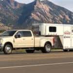 A white 2017 Ford F-350 used Ford diesel truck is towing a large horse trailer in front of a mountain.