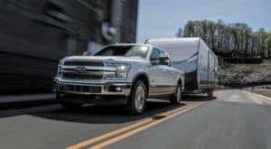 A white 2018 Ford F-150, a popular used Ford diesel truck, is towing a camper on a street.