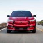 A red 2021 Ford Mustang Mach-E is shown from the front on a highway after leaving an Albany car dealer.