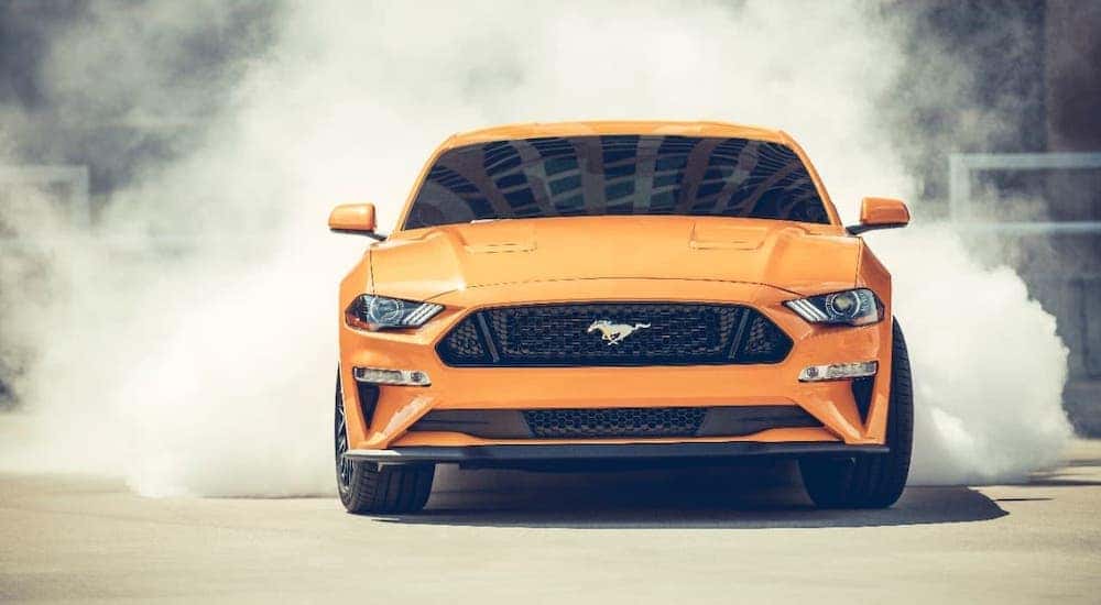 An orange 2018 Ford Mustang is shown from the front while smoke comes from the rear tires.