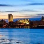 The Albany skyline is shown from across a river at dusk.