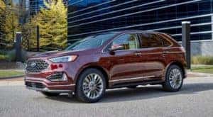 A dark red 2021 Ford Edge from a local Ford dealer is parked in front of glass buildings.