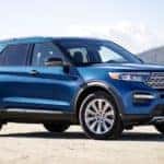A blue 2021 Ford Explorer from a local Ford dealer is parked in front of a lake and hills.