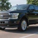 A black 2019 Ford F-150 from a used F-150 dealer is driving on a multi-lane road past a bay.