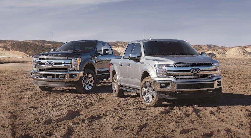 A black 2020 Ford Super Duty and a silver 2020 Ford F-150 are parked on a dirt lot after leaving a Schenectady used Ford dealer.