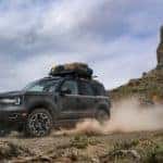 A black 2021 Ford Bronco Sport Outer Banks 4-door, a popular trim from your Ford Bronco Sport dealer, is shown driving on a dirt path away from a rock formation.