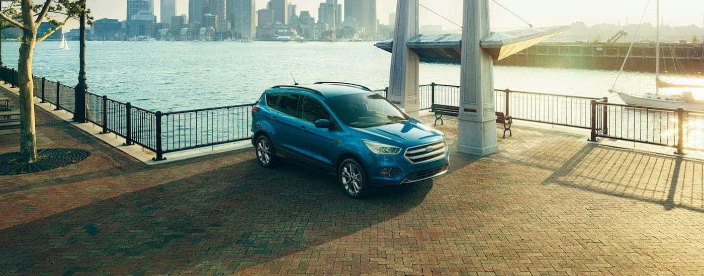 A blue 2017 Ford Escape Titanium is shown parked across a body of water from a city.