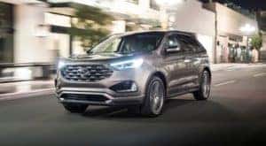 A silver 2019 Ford Edge is driving on a city street at night after leaving a NY certified pre-owned Ford dealer.