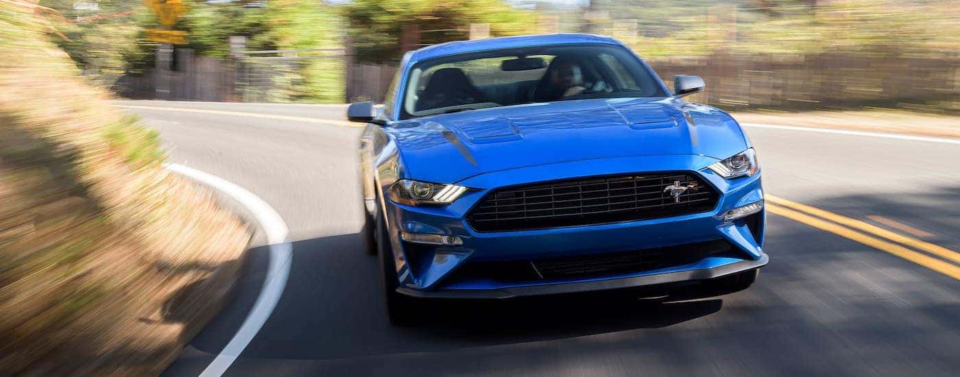 A blue 2019 Ford Mustang is shown from the front driving on a winding road.