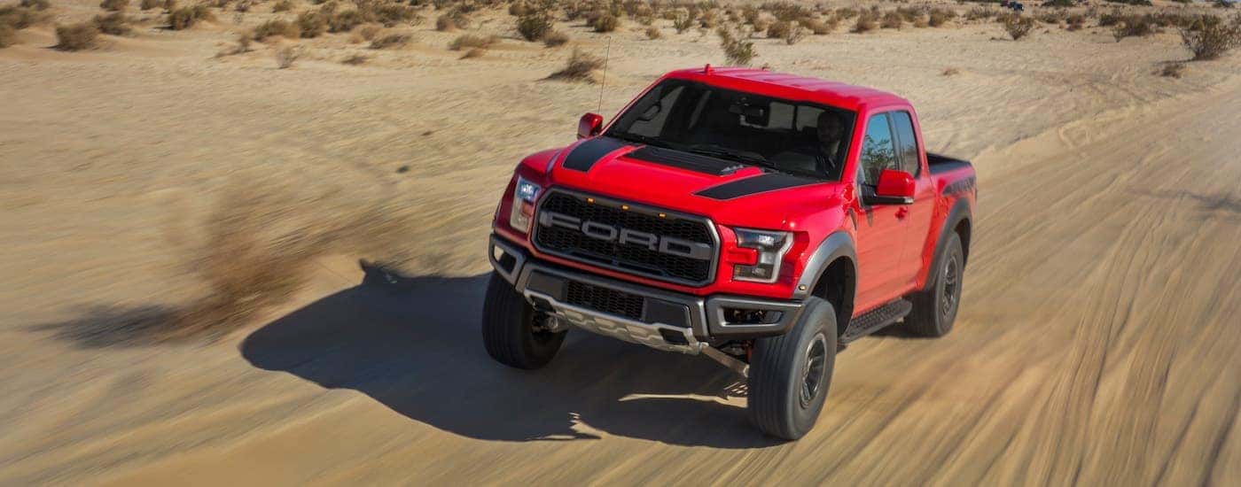 A red 2020 Ford F-150 Raptor is driving in the desert on sand.