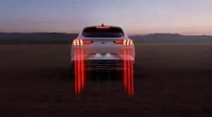 A white 2021 Ford Mustang Mach-E is shown from the rear with tail light streaks.