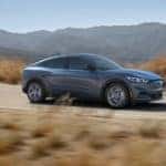 A grey 2021 Ford Mustang Mach-E Premium is driving through a desert road after leaving a Ford Mustang Mach-E dealer in Albany.