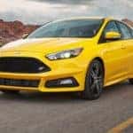 A yellow 2017 Ford Focus RS is driving past red rock hills.