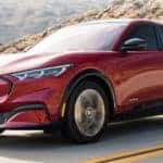 A red 2021 Ford Mustang Mach-E is driving down a two way road past the desert.