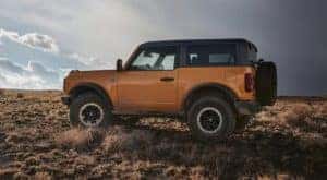 A yellow 2021 Ford Bronco two-door is parked off-road under a cloudy sky after leaving a NY Ford Bronco dealership.