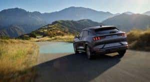 A grey 2021 Ford Mustang Mach-E is shown from the rear driving through the mountains after leaving a NY Ford Mustang Mach-E dealer.