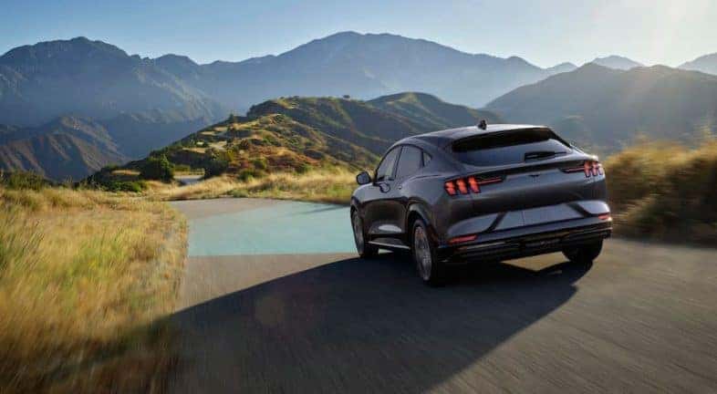 A grey 2021 Ford Mustang Mach-E is shown from the rear driving through the mountains after leaving a NY Ford Mustang Mach-E dealer.