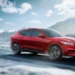 A red 2021 Mustang Mach-E is driving alone on a snowy road after leaving a NY Ford Mustang Mach-E dealer.