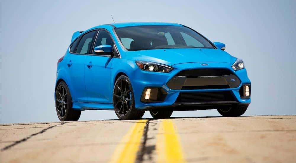A blue 2018 Ford Focus RS, part of Ford's car lineup, is shown from the front in the middle of the road.