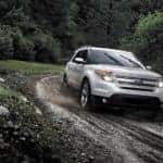 One of the most popular Ford pre-owned cars, a white 2014 Ford Explorer, is shown driving down a muddy path.