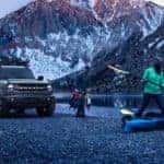 A grey 2021 Ford Bronco is shown on a shore in the mountains next to people going kayaking.