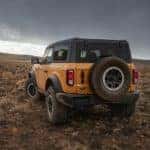 A yellow 2021 Ford Bronco is shown from the back off-roading at sunset.