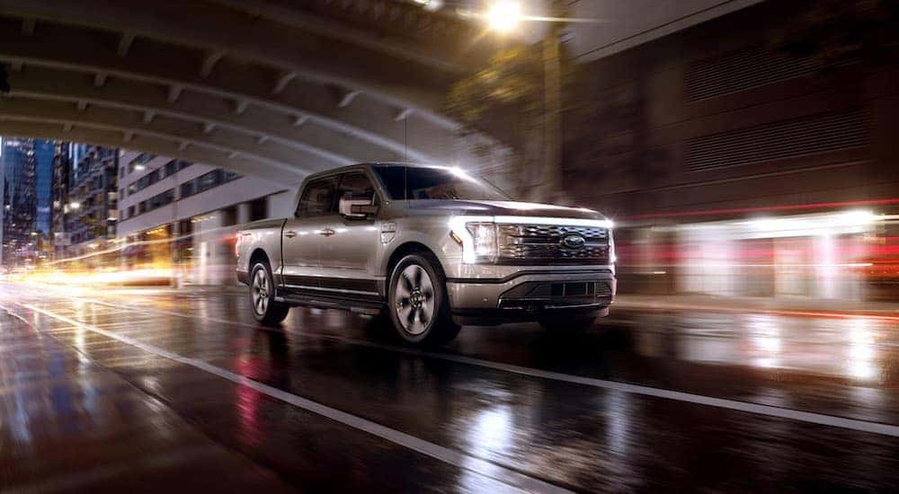 A silver 2022 Ford F-150 Lightning Platinum is shown driving on a wet city street at night after leaving a NY Ford delaer.