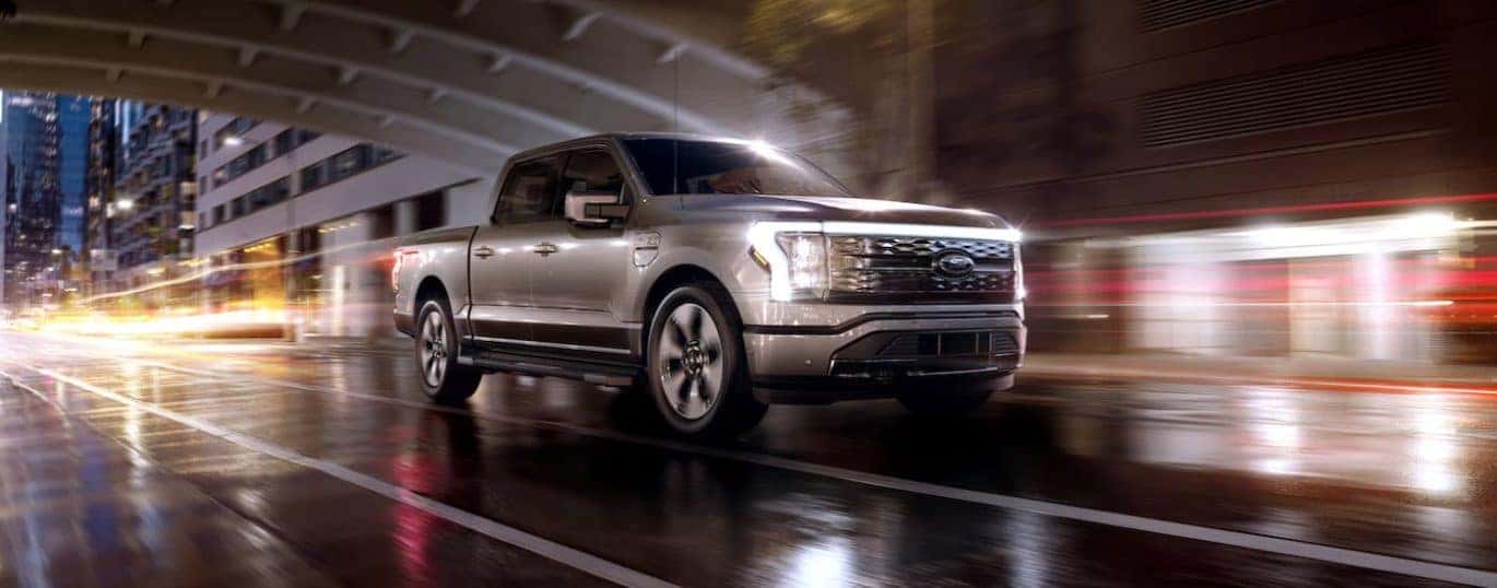 A silver 2022 Ford F-150 Lightning Platinum is shown driving in a city after winning a 2022 Ford F-150 Lightning vs 2022 Tesla Cybertruck comparison.
