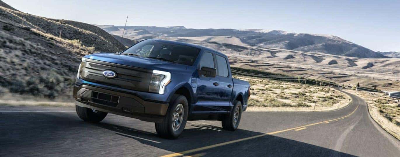 A blue 2022 Ford F-150 Lightning Pro is shown driving down a deserted road.