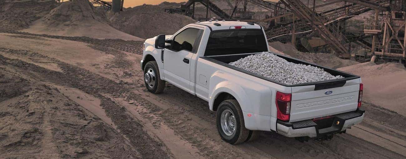 A white 2022 Ford F-350 is hauling a load of crushed stone through a fill yard.