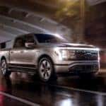 A grey 2022 Ford F-150 Lightning is shown driving through a city after leaving a Ford dealer in Schenectady, NY.