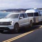 A white 2022 Ford F-150 Lightning is shown towing an Airstream after leaving an electric car dealer in Albany.