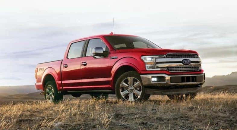 A red 2020 Ford F-150 is shown parked in a dry grassy field near a certified pre-owned Ford F-150 dealer.