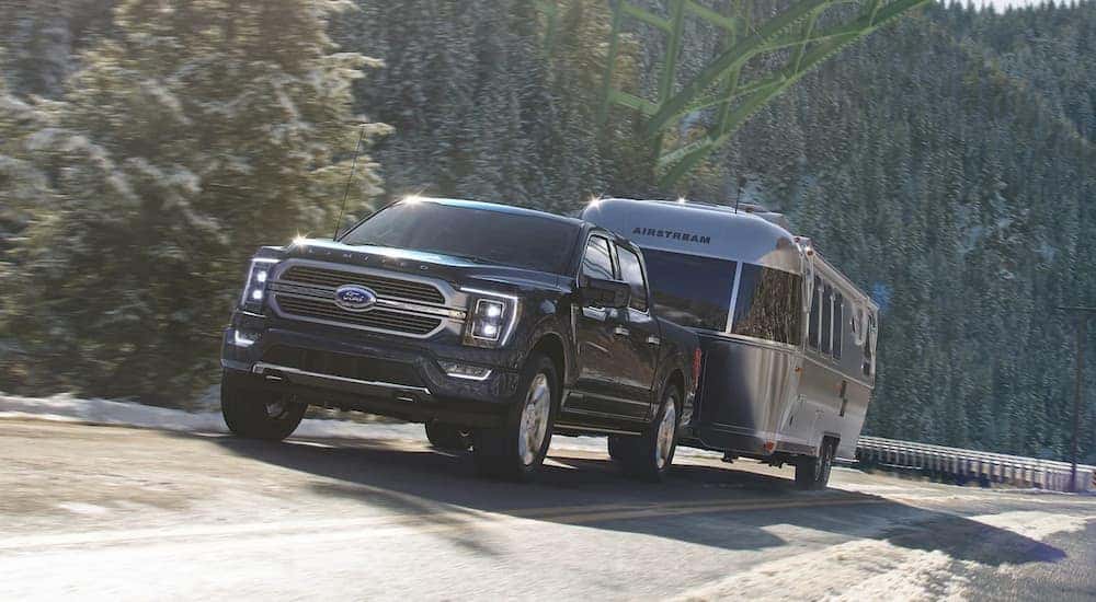A black 2021 Ford F-150 Limited is shown towing a silver camper.