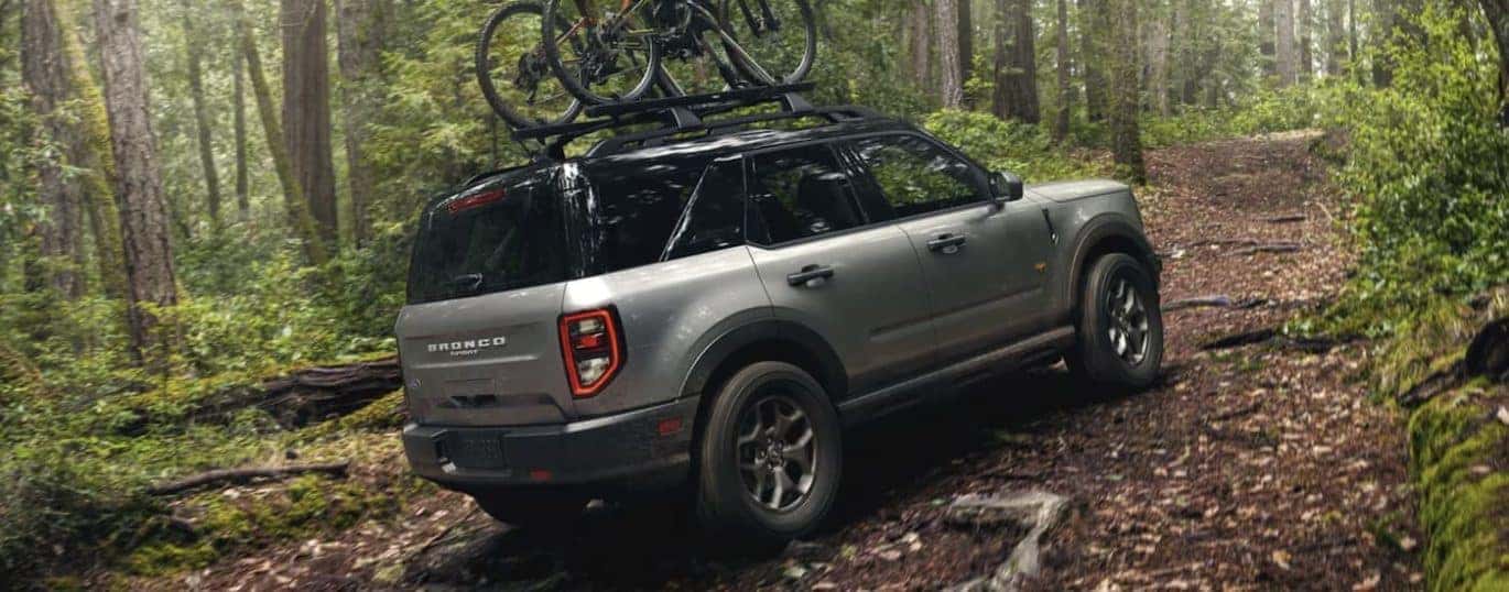 A silver 2022 Ford Bronco Sport is shown from the side off-roading in the woods with bikes mounted on the roof.