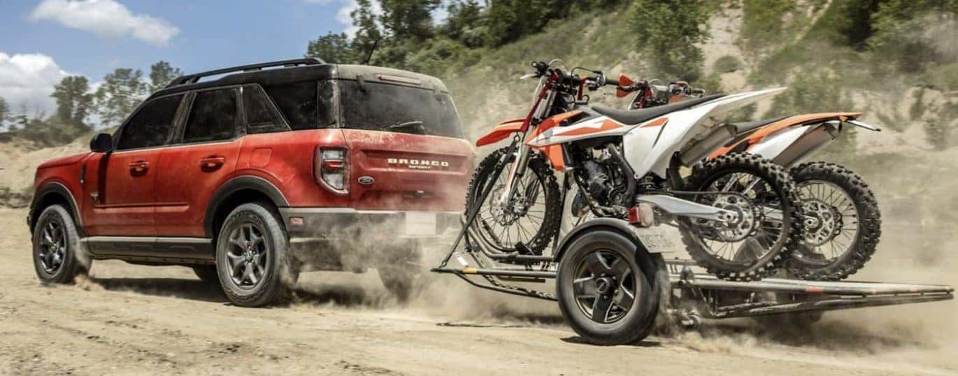 A red 2022 Ford Bronco Sport is shown towing a trailer with dirt bikes on a dirt road.