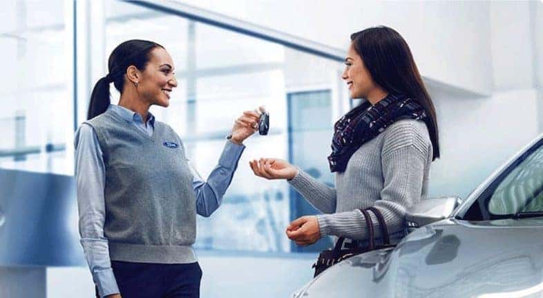 A customer is shown speaking to a saleswoman at a certified pre-owned Ford dealership.
