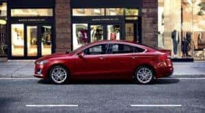 A red 2020 Ford Fusion is shown parked on a city street near a used car dealership in Albany.