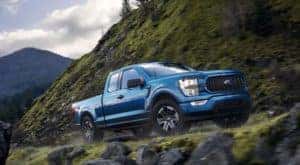 A blue 2021 Ford F-150 STX is shown driving on a mountain road.