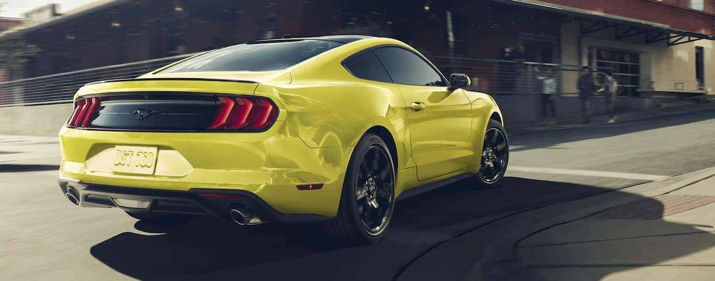 A yellow 2021 Ford Mustang is shown from the rear driving on a city street.