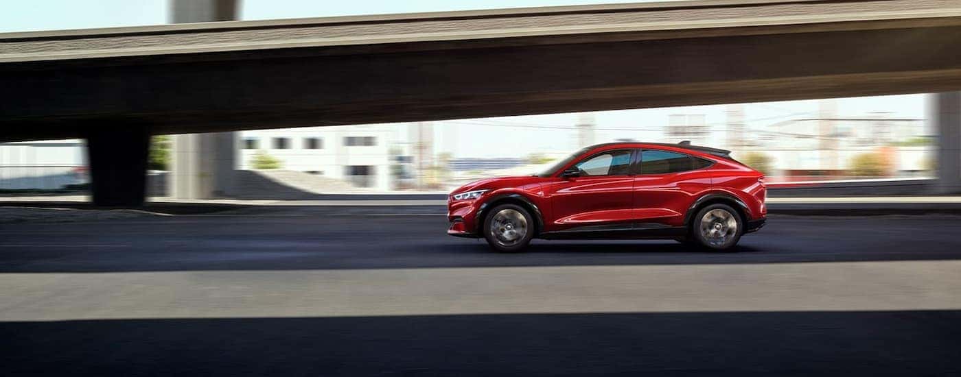 A red 2022 Ford Mustang Mach-E Premium is shown from the side driving past a bridge.