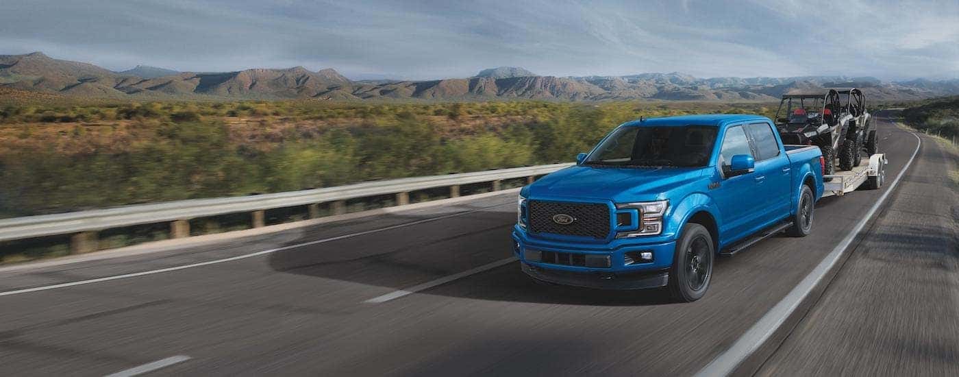 A blue 2020 Ford F-150 XLT is shown towing a boat after leaving a Troy Ford dealership.