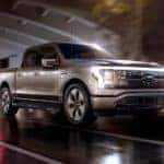 A silver 2022 Ford F-150 Lightning is shown driving through a city at night.