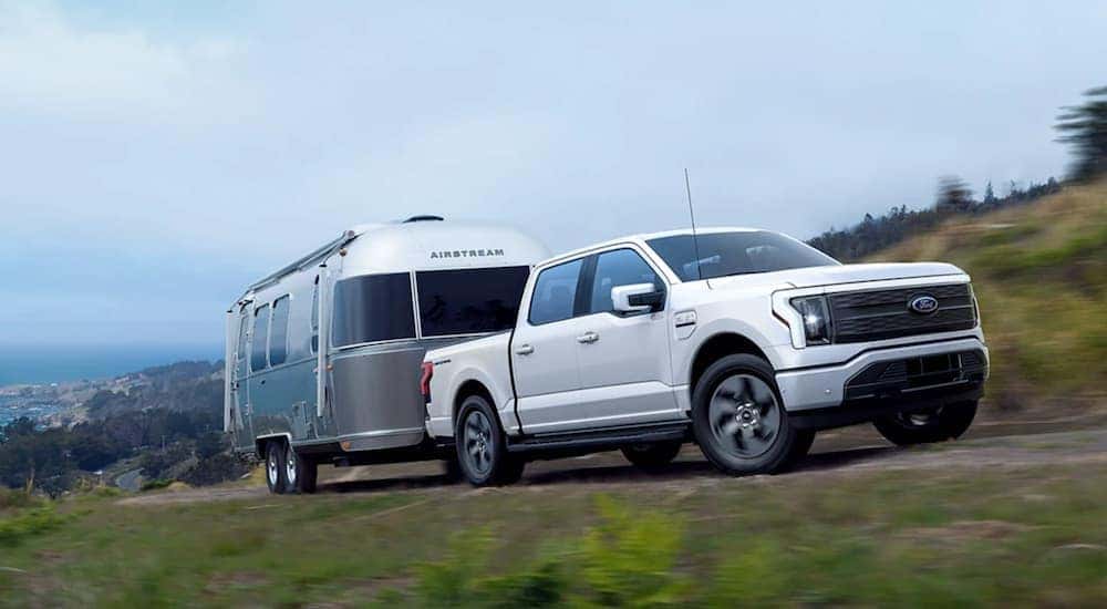 A white 2022 Ford F-150 Lightning is shown towing an airstream trailer.