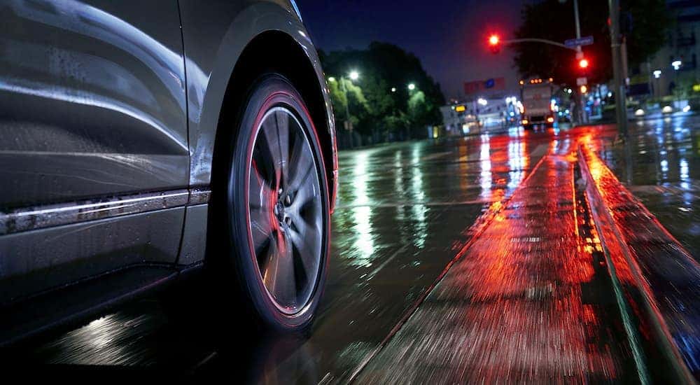 A close up shows a wet street, traffic lights, and the wheel of a grey 2014 Ford Edge.