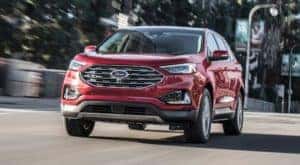 A maroon 2019 Ford Edge Titanium is shown from the front driving on a city street after visiting a used Ford Edge dealer.