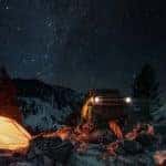 A yellow 2022 Ford Bronco is shown parked near a tent on a starry night.