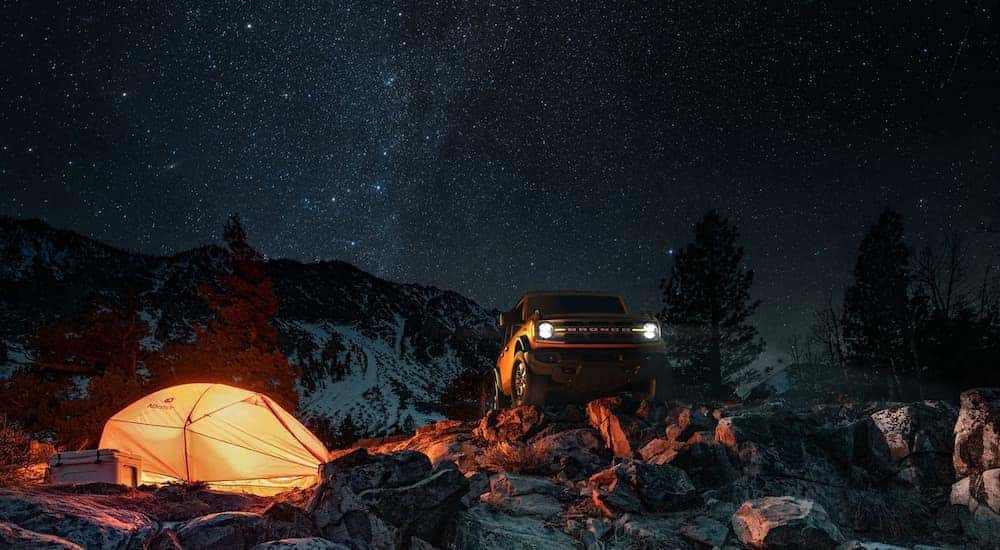 A yellow 2022 Ford Bronco is shown parked near a tent on a starry night.